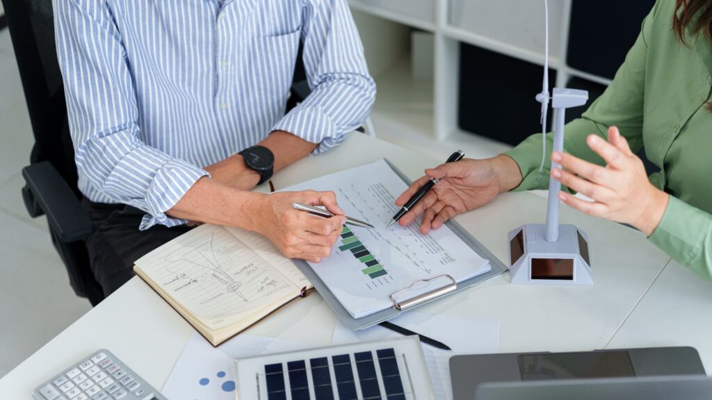 Hände erwachsener asiatischer Geschäftsleute, die ESG-Finanzdaten und Projektpläne für erneuerbare Energien analysieren